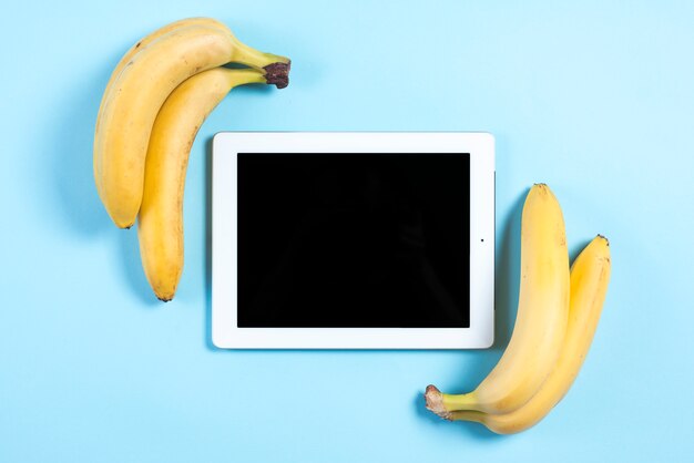 Plátanos amarillos cerca de la tableta digital sobre fondo azul