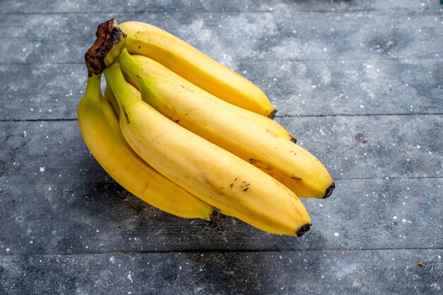 Plátanos amarillos frescos bayas enteras sobre gris, sabor a vitamina baya de fruta