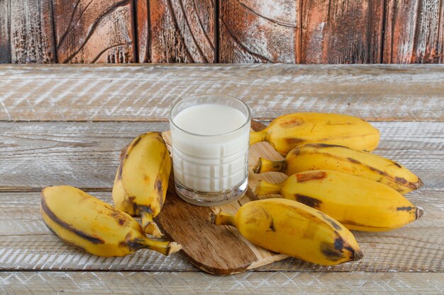 Plátanos con leche en madera y tabla de cortar, vista de ángulo alto.