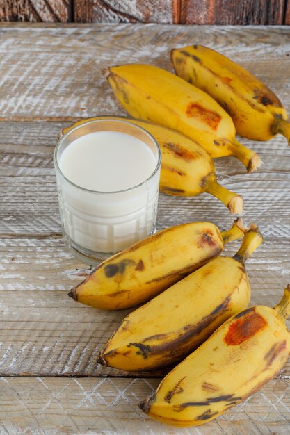 Plátanos maduros con leche en madera, vista de ángulo alto.