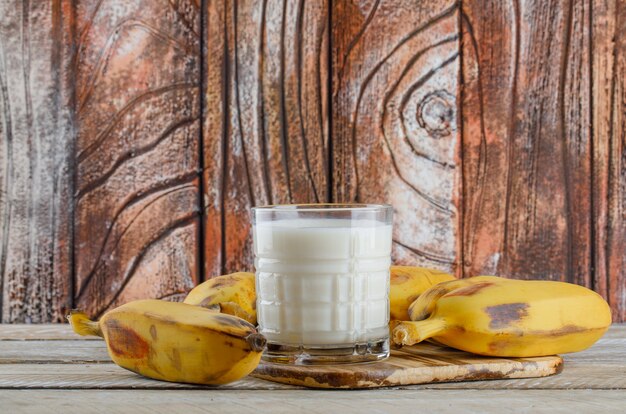 Foto gratuita plátanos con vista lateral de leche en madera y tabla de cortar