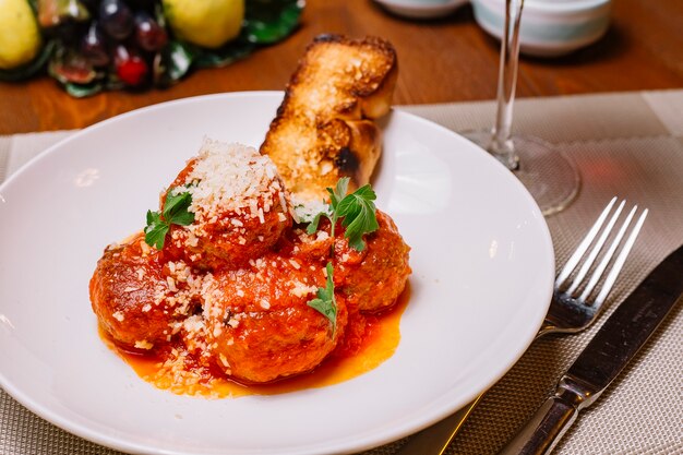 Plato de albóndigas adornado con salsa de tomate, parmesano rallado y perejil servido con tostadas