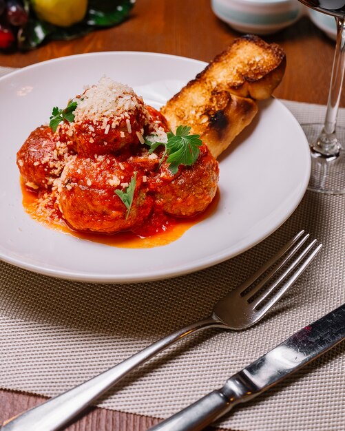 Plato de albóndigas adornado con salsa de tomate, parmesano rallado, perejil y tostadas