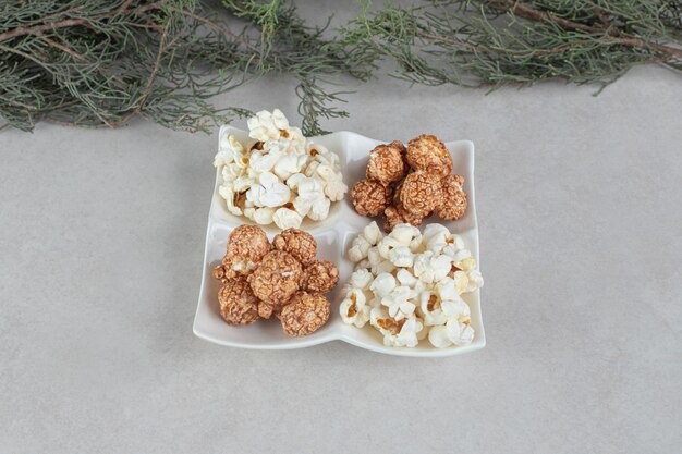 Plato de aperitivo lleno de porciones de palomitas de maíz variadas y ramas de árboles de hoja perenne sobre una mesa de mármol.