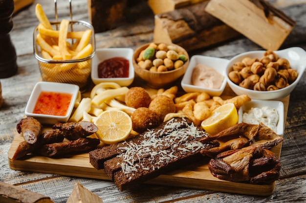 Plato de aperitivos con alas ahumadas salchichas papas fritas nueces y salsas