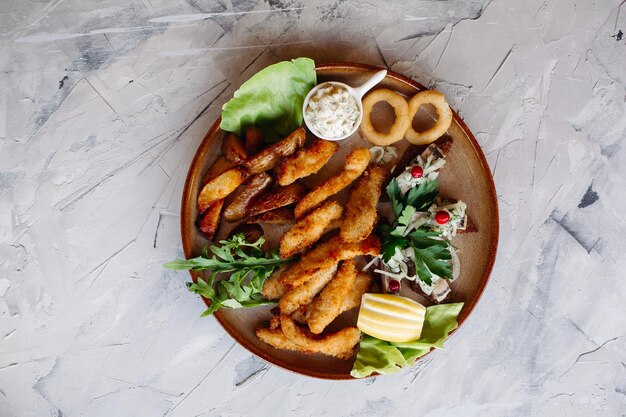 Plato de arcilla lleno de aperitivos, incluidos nuggets de pollo dorados con corteza crujiente, deliciosos canapés con arenque y tomates cherry servidos con salsa de ajo decorada con hojas de ensalada y queso