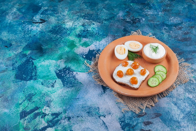 Plato de arcilla de pan de molde con crema blanca y mermelada de bayas sobre superficie azul.