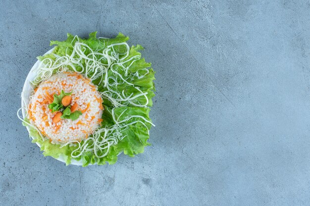 Plato de arroz cocido decorado con queso y lechuga sobre mármol.