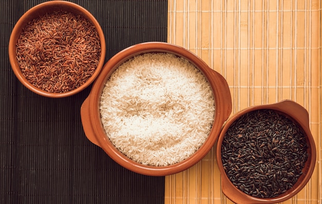 Plato de arroz rojo jazmín; arroz blanco y cuencos de arroz negro en la estera de lugar