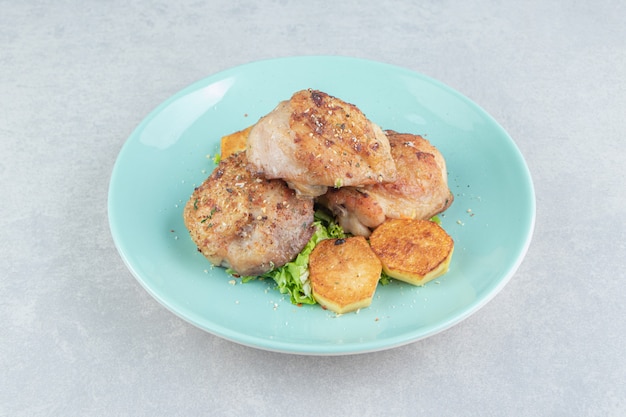 Un plato azul de carne con patatas fritas en rodajas y lechuga.