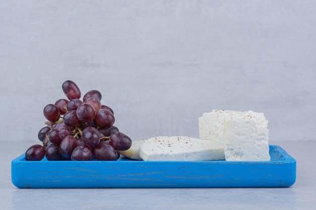 Un plato azul lleno de queso blanco y uvas moradas. Foto de alta calidad