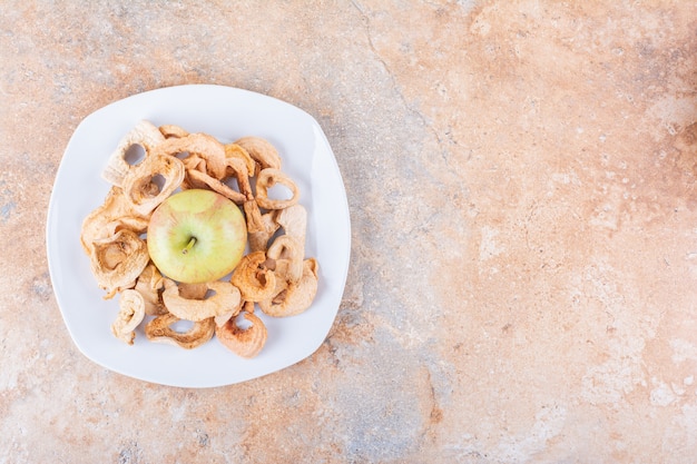 Plato blanco de anillos de manzana seca y manzana verde fresca sobre mesa de mármol. Foto de alta calidad