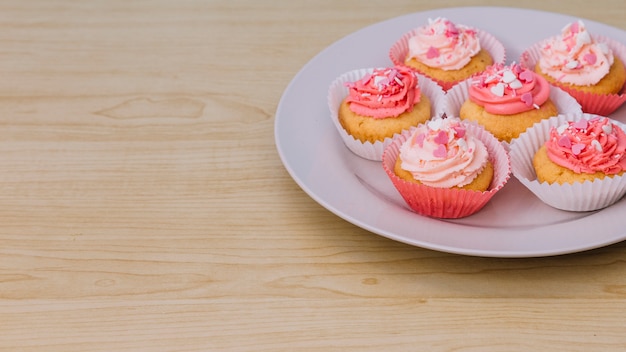 Plato blanco con crema de cupcake y rociado en escritorio de madera