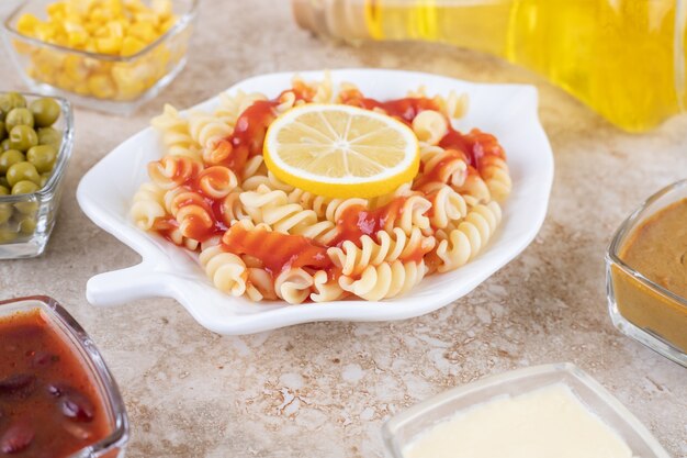 Un plato blanco de deliciosa pasta espiral con rodaja de limón