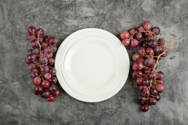 Plato blanco y deliciosas uvas rojas sobre mesa de mármol.