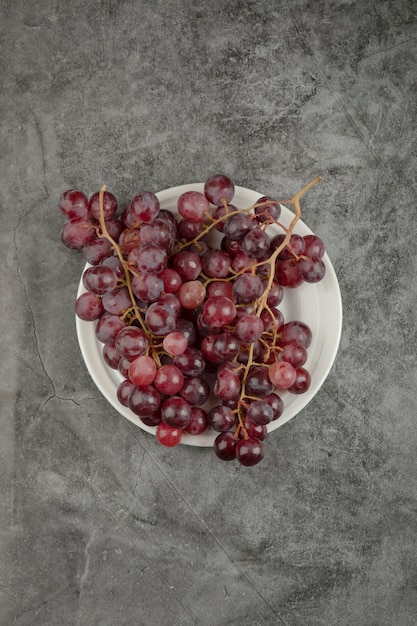 Plato blanco y deliciosas uvas rojas sobre mesa de mármol.