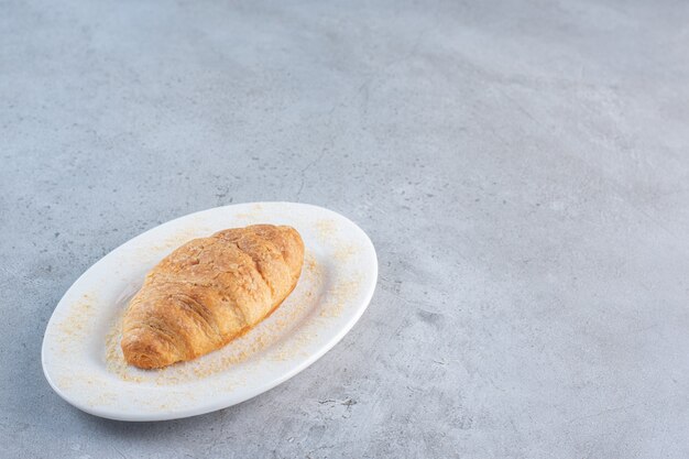 Un plato blanco de delicioso croissant dulce sobre fondo azul.