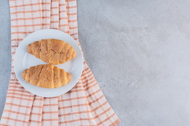 Un plato blanco de deliciosos croissants dulces sobre un mantel rayado.