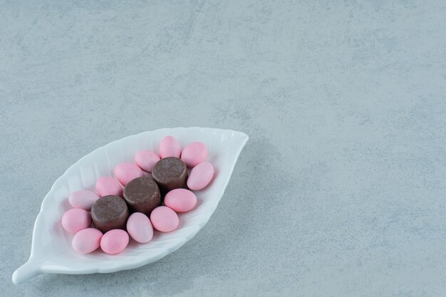 Un plato blanco con dulces caramelos de color rosa y galletas de chocolate en la superficie blanca