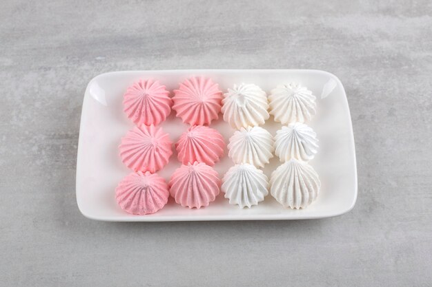 Plato blanco de dulces de merengue blanco y rosa en la mesa de piedra.
