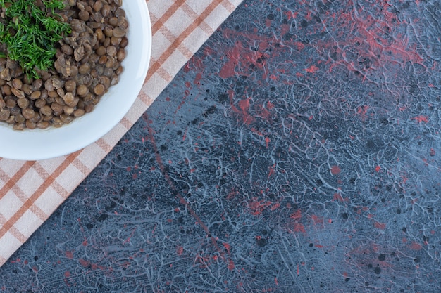 Un plato blanco con frijoles y hierbas sobre un mantel.