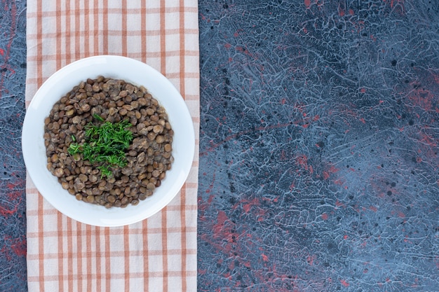 Un plato blanco con frijoles y hierbas sobre un mantel