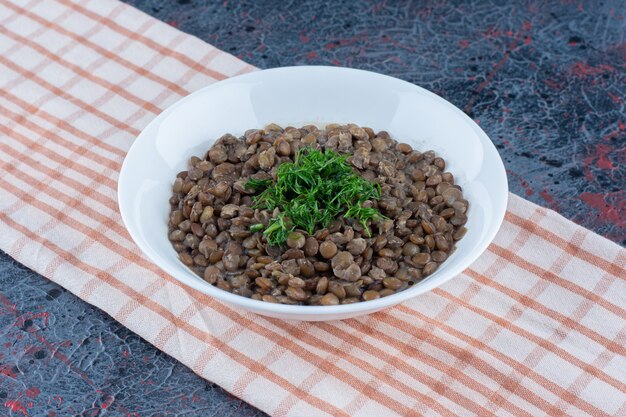 Un plato blanco con frijoles y hierbas sobre un mantel