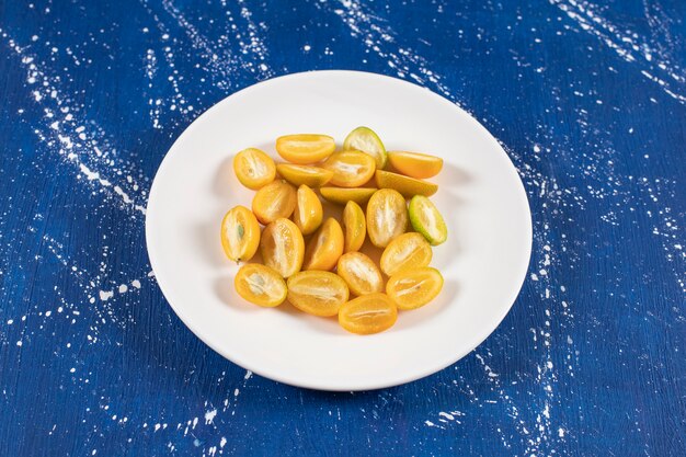 Plato blanco de frutas kumquat frescas en rodajas sobre superficie de mármol