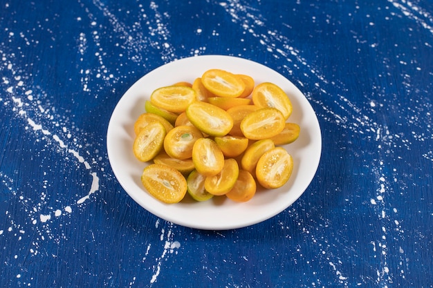 Plato blanco de frutas kumquat en rodajas sobre superficie de mármol