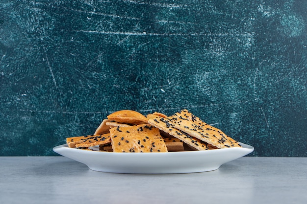 Plato blanco de galletas crujientes con semillas negras sobre fondo de mármol.