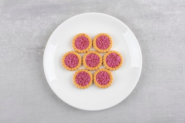 Plato blanco de galletas dulces con chispitas rosas sobre piedra.