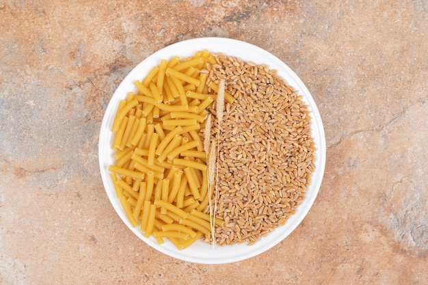 Un plato blanco de granos y trigo con macarrones crudos sobre fondo de mármol. Foto de alta calidad