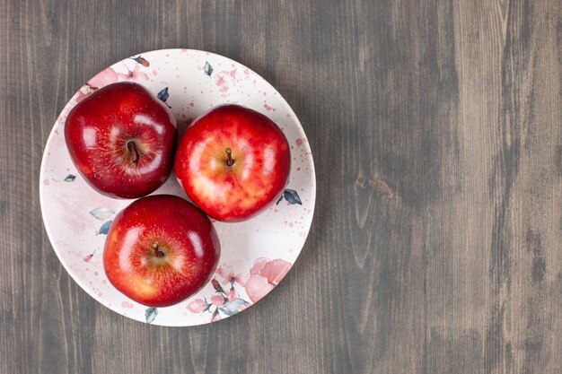 Un plato blanco con jugosas manzanas rojas sobre una mesa de madera. Foto de alta calidad