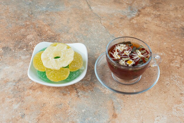 Un plato blanco lleno de caramelos de gelatina de azúcar y una taza de té de hierbas