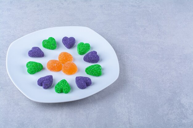 Un plato blanco lleno de caramelos de gelatina azucarada en la mesa gris.