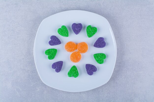 Un plato blanco lleno de caramelos de gelatina azucarada sobre superficie gris