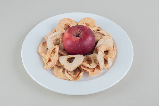 Un plato blanco lleno de manzanas secas con una manzana entera.