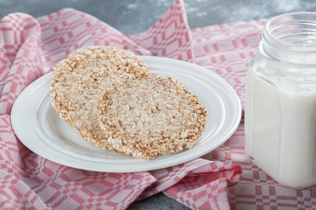 Un plato blanco lleno de pan de arroz inflado con un tarro de leche.