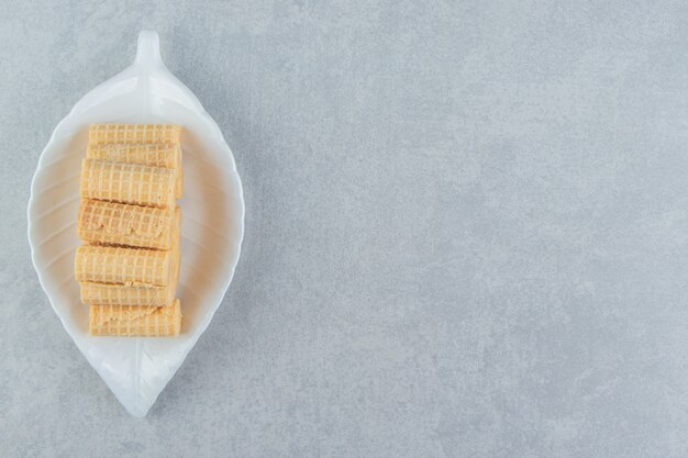 Un plato blanco lleno de rollos de gofres crujientes.