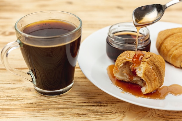 Plato blanco con miel y cruasanes y una taza de café.