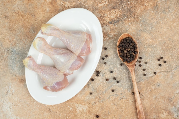 Foto gratuita un plato blanco con muslo de pollo crudo con cuchara de madera de pimienta