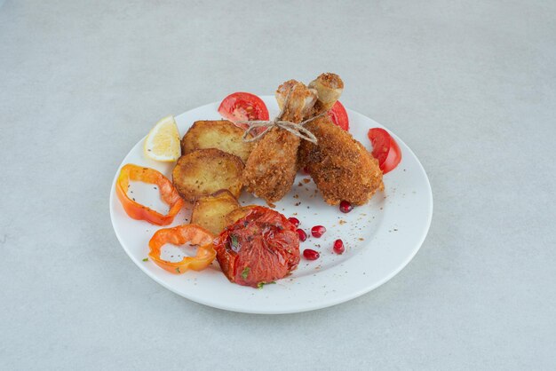 Un plato blanco de pollo frito y patatas con pimiento en rodajas.