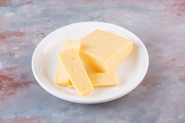 Plato blanco de rodajas de queso amarillo sobre superficie de mármol.