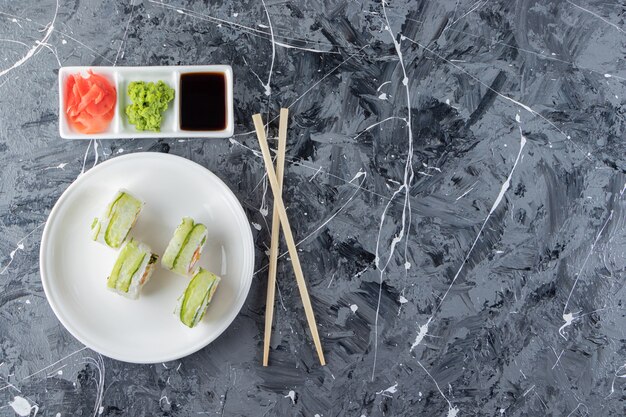 Plato blanco de rollos de sushi dragón verde sobre fondo de mármol.