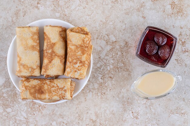 Un plato blanco de sabrosas crepas y mermelada de fresa.