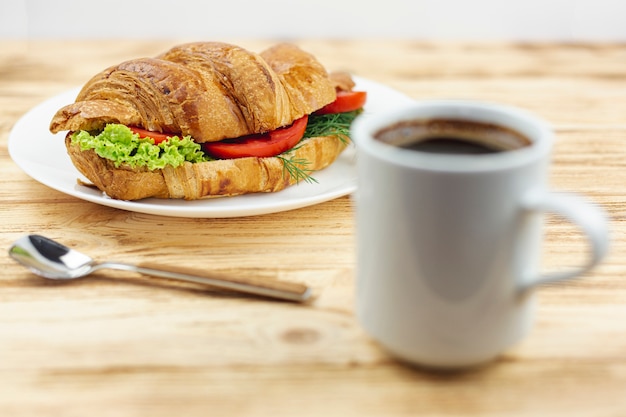 Plato blanco con un sandwich y una taza de café sobre una mesa de madera