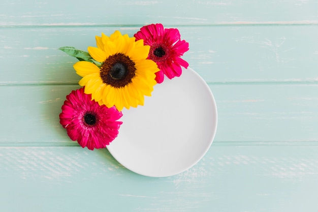 Plato blanco vacío decorado con flores de girasol y gerbera en la mesa