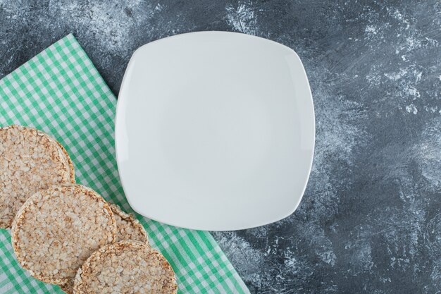 Un plato blanco vacío con pan de arroz crujiente sobre una superficie de mármol.