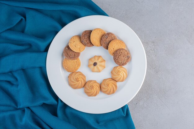 Plato blanco de varias galletas dulces sobre fondo de piedra.