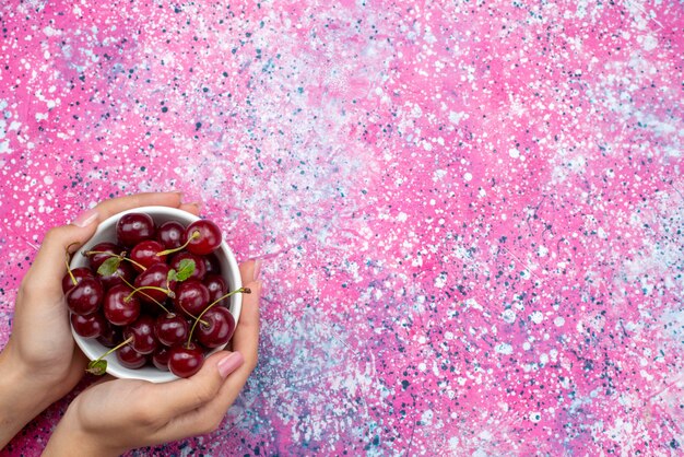 Plato blanco de vista superior con cerezas frescas rojas agrias sosteniendo por la hembra en el fondo de color brillante fruta color agrio